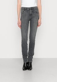 Vaqueros ajustados de mezclilla gris con cintura media, bolsillos frontales y detalles de costura, combinados con botas negras a los tobillos. Textura suave.