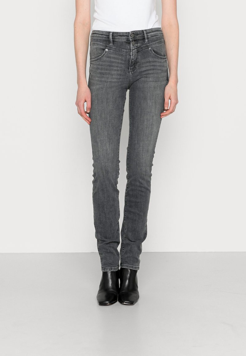 Vaqueros ajustados de mezclilla gris con cintura media, bolsillos frontales y detalles de costura, combinados con botas negras a los tobillos. Textura suave.