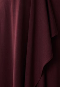 Bordeaux stof met een gladde, matte textuur, elegant gedrapeerd om zachte plooien en zachte contouren te tonen. Geen zichtbare patronen of hardware.