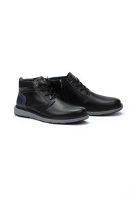 Botas de cuero negras hasta el tobillo con suelas de goma gris, con cordones, panel lateral en contraste y cierre con cremallera para facilitar su uso.