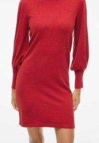 Vestido de punto rojo con mangas abullonadas largas y escote redondo, que presenta una silueta ajustada y puños acanalados para mayor textura.
