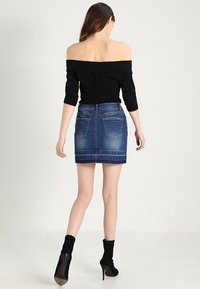 Haut noir décolleté avec manches trois-quarts, associé à une mini-jupe en denim bleu avec deux poches arrière et un ourlet effiloché.