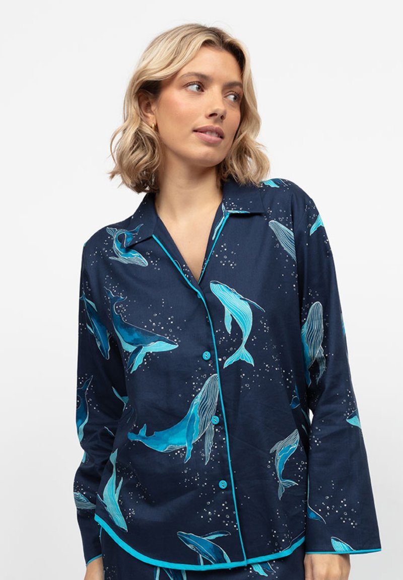 Camicia navy con maniche lunghe, stampa di balene turchesi, piping in contrasto turchese e chiusura con bottone. Tessuto morbido con una texture liscia.