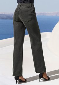 Jeans neri a vita alta con gambe dritte, dotati di tasche posteriori e una consistenza morbida. Abbinati a tacchi aperti neri.