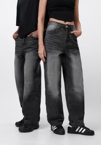 Grå denimjeans med avslappet passform, med en falmet vask, fem-lomme-design og synlige sømdetaljer. Bæres med svarte sneakers.