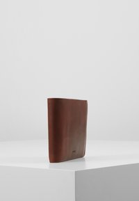 Bruine leren portemonnee met een gladde textuur, slanke rechthoekige vorm en subtiele branding aan de voorkant. Minimalistisch ontwerp zonder zichtbare hardware.