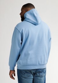 Světle modrá mikina vyrobená z bavlněné směsi, má klokaní kapsu, žebrované manžety a kapuci na šňůrky. V kombinaci s modrými džínami.