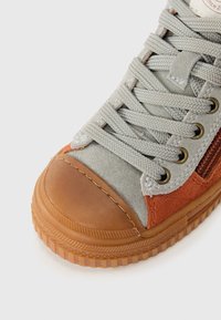 Grå og oransje semsket sneakers med gummitåhette, teksturerte snørebånd, gulløyer og en rillet gummisåle.