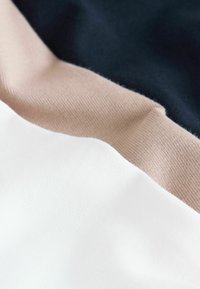 Textiles en blanc, beige et marine, disposés en couches superposées. Le tissu présente une texture lisse avec un motif en maille fine.