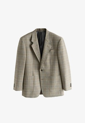 Person justerer manchet på beige og brun ternet blazer, båret over hvid skjorte og blå jeans.