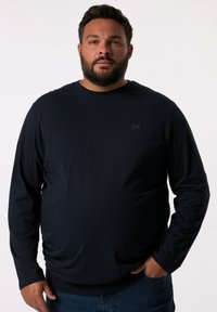 Granatowa koszula z długim rękawem i okrągłym dekoltem, wykonana z miękkiej tkaniny. Posiada minimalistyczne logo na piersi oraz ściągacze przy rękawach i u dołu.