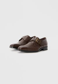 Zapatos de cuero marrón con un acabado liso y un patrón texturizado de cocodrilo en la correa, con una hebilla de metal y un tacón bajo.