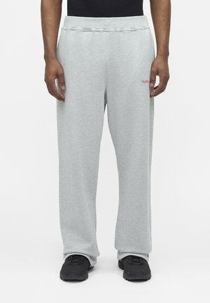 Pantaloni della tuta grigio chiaro con vita elastica e piccolo testo rosso "No Problem" sulla parte superiore della coscia sinistra, indossati con scarpe da ginnastica nere.