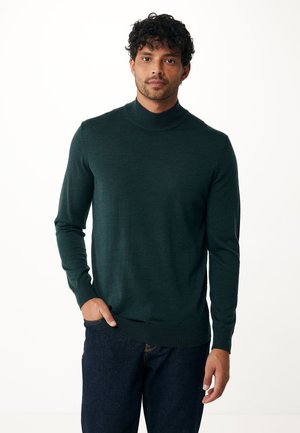 Dunkelgrüner Rollkragenpullover aus einem weichen Strickstoff, taillierte Passform, lange Ärmel und gerippte Bündchen sowie Saum. Trägt man über einer dunklen Jeans.