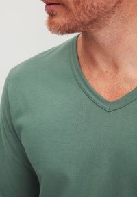 Groene V-hals t-shirt gemaakt van zacht katoen, met een gladde textuur en subtiele naden langs de halslijn.