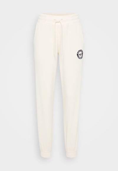 Cremfarbene Jogginghose mit elastischem Bund, Kordelzug und einem runden, gestickten Logo auf der linken Hüfte. Weicher, glatter Stoff, eng zulaufendes Bein.