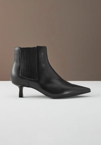 Černá kožená kotníková bota s špičatou špičkou a malým podpatkem. Obsahuje žebrované elastické boční panely pro snadné oblékaní a hladký povrch.