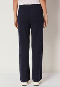 Marinblå vida byxor tillverkade av mjukt tyg med elastisk midja. Rak passform, slät textur och minimala sömnadsdetaljer.