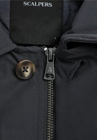 Black jacket with a smooth, matte finish; features a zippered front closure, branded button, and high collar design.