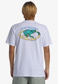 Camiseta blanca de algodón con un gráfico colorido de una rana verde sobre un símbolo de paz, con el texto "MANTEN LA PAZ" arriba.
