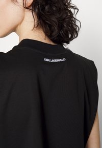 Camiseta negra de manga corta con cuello redondo y un logo blanco bordado visible de "KARL LAGERFELD" en la parte trasera.