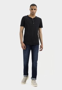 Black cotton henley shirt with three buttons, paired with dark denim jeans and light grey sneakers. Simple, fitted design.