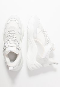 Chaussures de sport blanches en mesh et daim, dotées d'une semelle épaisse, d'accents texturés et d'un design minimaliste.