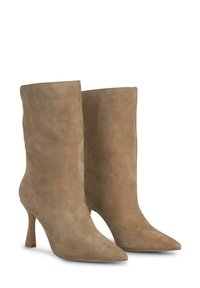 Bottines en daim beige, avec un bout pointu et un talon aiguille de 7,5 cm. Texture lisse avec un design simple et des lignes épurées.