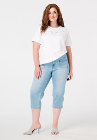 T-shirt blanc à manches courtes avec des détails en dentelle, associé à un jean cropped bleu clair et des mules à talons bleu clair. Design simple, coupe décontractée.