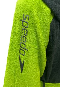 Accappatoio verde in spugna con cappuccio nero, caratterizzato dalla parola "Speedo" in grigio sulla manica e una texture liscia e morbida.