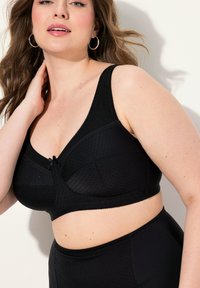 Zwarte beha met een gestructureerd oppervlak, voorzien van een diepe V-vorm, brede bandjes en een klein strikje in het midden.