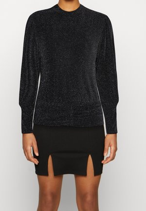 Haut noir à manches longues scintillant associé à unemini-jupe noire avec des fentes centrales avant et latérales.