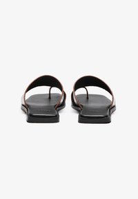 Sandales plates noires avec deux larges sangles, design minimaliste, texture lisse et accent brun contrastant le long des bords.