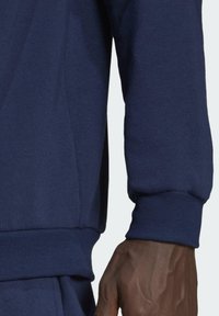 Manche de sweat-shirt bleu marine montrant un tissu doux et texturé avec des poignets côtelés ; vue rapprochée mettant en évidence les coutures et une main.