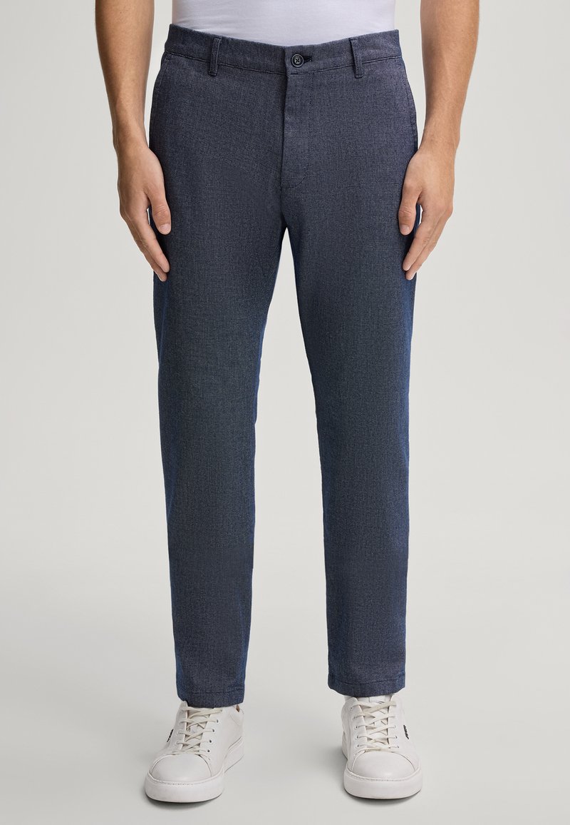 Pantaloni blu scuro con un motivo testurizzato, dotati di chiusura a bottone e tasche laterali. Abbinati a sneaker bianche per un contrasto.