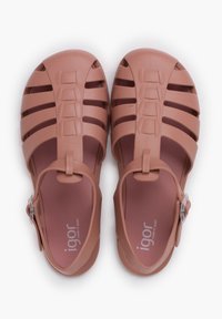 Pink plastic sandals featuring a cut-out pattern, adjustable strap, and an embossed logo. Soles are flat with a smooth texture.