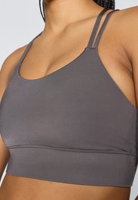 Sutiã desportivo cinza feito de um tecido suave, apresentando alças duplas finas e um design sem costuras com decote arredondado e faixa sob o busto.