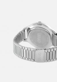 Sølv rustfrit stål armbåndsur med en poleret led forbundet, rund urkasse og en struktureret krone. Bagsiden har indgraverede detaljer og urværket er vandtæt.