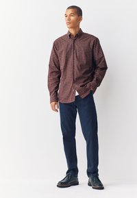 Camicia a quadri rossa, blu e bianca con colletto con bottoni; abbinata a pantaloni di jeans blu scuro e scarpe nere.