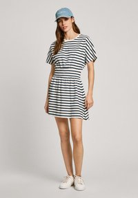 Dryžuota suknelė su prigludusia juosmens dalimi, trumpomis rankovėmis ir plačiu sijonu. Spalvos: balta ir tamsiai mėlyna. Suderinta su šviesiai mėlynu kepurėle ir baltais sportbačiais.