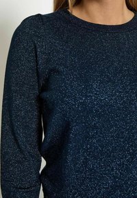 Granatowy sweter z dzianiny z teksturowanym, błyszczącym wykończeniem, okrągłym dekoltem i długimi rękawami z delikatnym bufiastym detalem na ramionach.