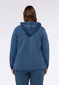Blauer Hoodie mit einem Kordstoffgefühl an der Kapuze. Verfügt über gestickte Designs auf den Ärmeln. Insgesamt glattes Material, lässige Passform.