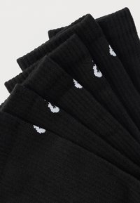 Πέντε ζευγάρια μαύρες ριγωτές κάλτσες με μικρά λευκά λογότυπα φλόγας κοντά στο πάνω μέρος της μανσέτας, τοποθετημένα αλληλοκαλυπτόμενα σε λευκό φόντο.