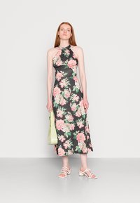 Vestido midi floral com decote halter, fundo preto, flores rosa e verdes. Combinado com sandálias de salto alto cor de rosa claro e uma bolsa verde.