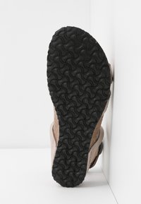 Suola di una scarpa con una suola in gomma nera testurizzata con un motivo ondulato. Parte superiore color marrone chiaro, che mostra una combinazione di materiali.