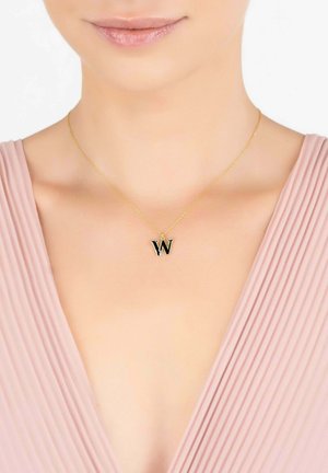Gold chain necklace featuring a black letter "W" pendant, worn on a light pink, pleated garment. Simple design with polished finish.