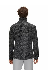 Uomo che indossa una giacca in pile grigio scuro con una alta collarino e pantaloni grigio chiaro, visto da dietro su uno sfondo bianco.