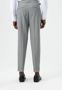 Grijze geruite broek met een getailleerde pasvorm, voorzien van twee achterzakken en opgerolde pijpen, gecombineerd met zwarte schoenen en een wit overhemd.