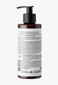 Bouteille en plastique ambré foncé avec pompe, 300 ml, munie d'un couvercle à pompe noir. Présente une étiquette blanche mate texturée avec les informations sur le produit et les ingrédients.