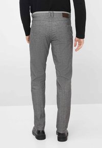 Grijze, textuurlijke broek met een rechte snit en achterzakken, met een bruine leren patch op de tailleband en zwarte schoenen.